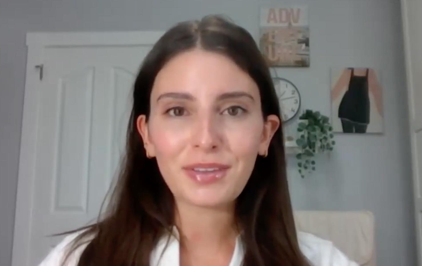 Carla Bezanson speaks to a webcam. She has long dark hair and a white shirt.