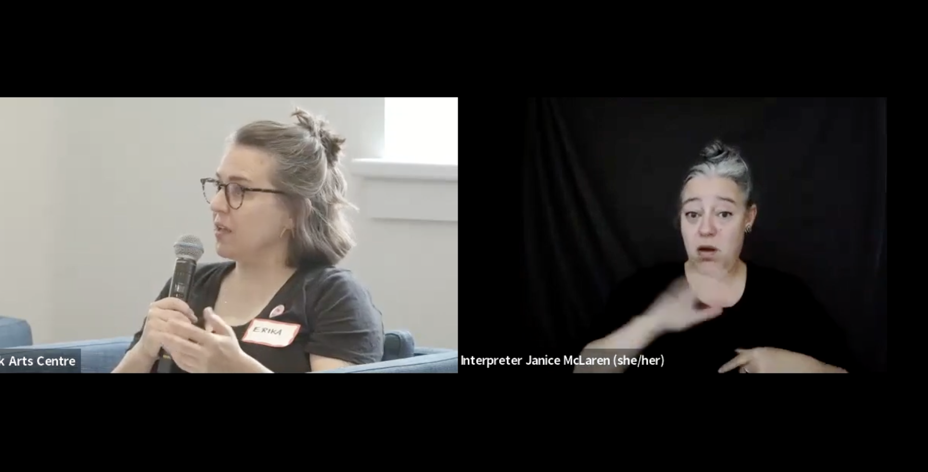 Erika Shea and ASL Interpreter Janice McLaren speak on a screen. Erika is holding a microphone and addressing the room.